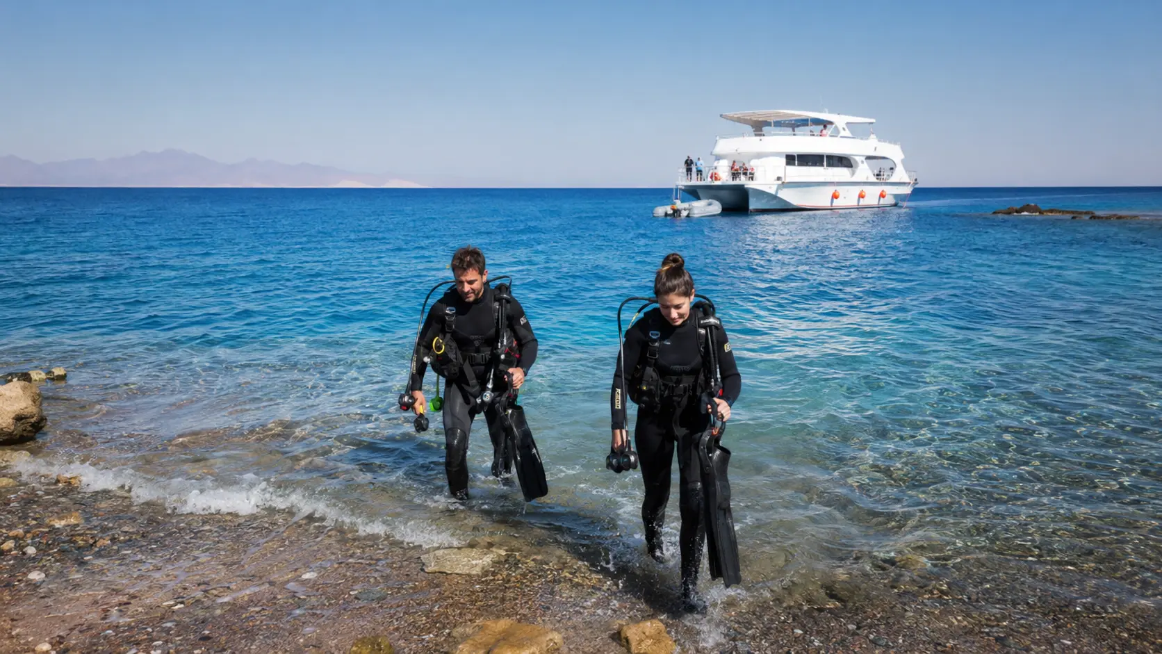 Scuba divers entering from shore with a dive boat offshore in Hurghada